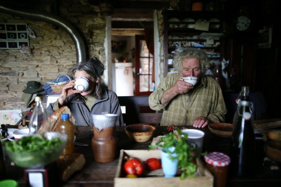 Laurence and Jean-Bernard sip from cups in their farmhouse