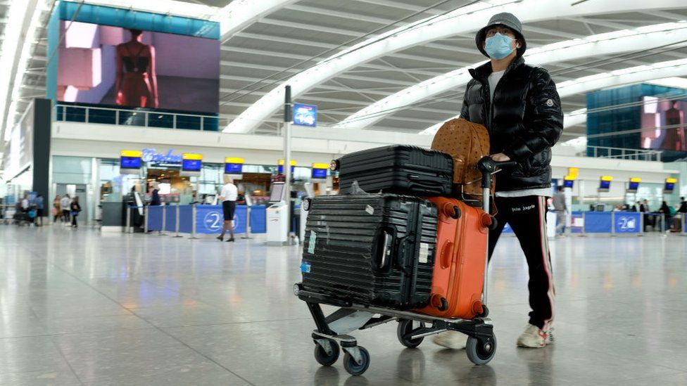 Man wearing mask pushes trolley through airport