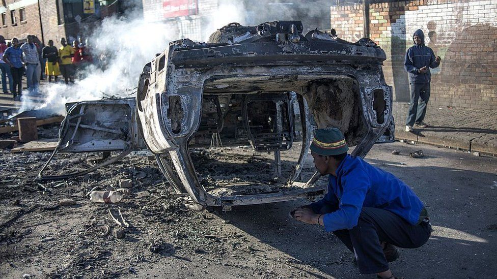 People look at a burnt-out car torched in the early hours outside the Jeppies Hostles, in the Jeppestown area of Johannesburg, on 17 April 2015