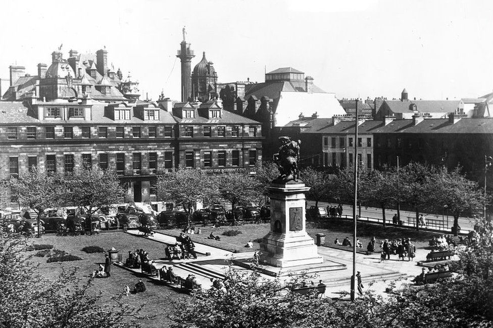 A black and white picture of a a town square with a statue in the middle surrounded by terraced homes