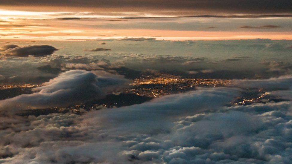 Mar de nubes blancas y un horizonte rojizo sobre las luces de una ciudad