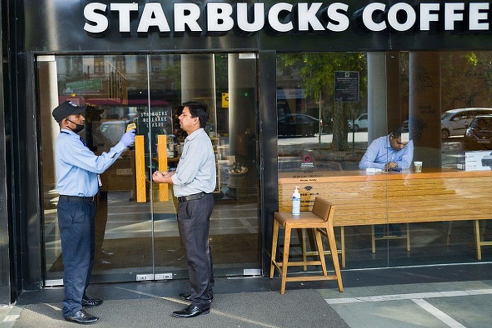 A security guard (L) takes the temperature of a patron as a preventive measure against the COVID-19 novel coronavirus before he enters a Starbucks coffee shop in New Delhi on March 17, 2020