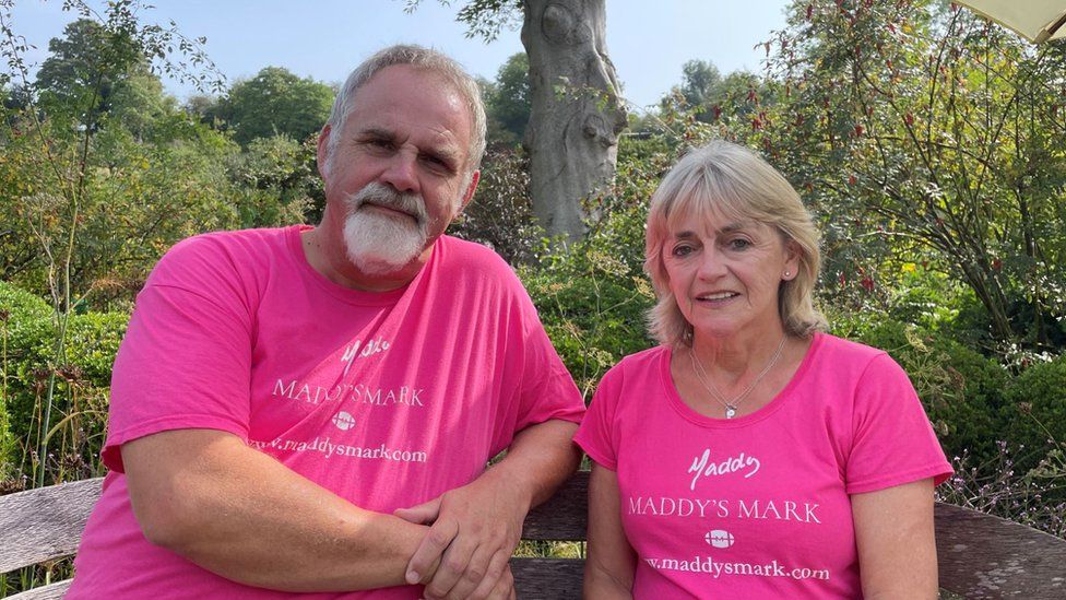 Simon and Karen, Maddy's parents, sitting on a bench wearing pink Maddy's Mark t-shirts