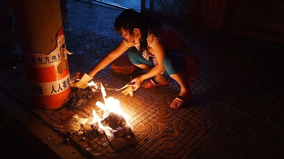 This photo taken on August 7, 2014 shows a woman burning paper money to pay respects to deceased ancestors and loved ones during the Ghost Festival, on a sidewalk outside a restaurant in Ludian, in China's southwest Yunnan province.