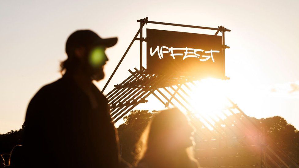 The silhouette of a man wearing a hat at sunset, standing in front of a sign that reads Upfest