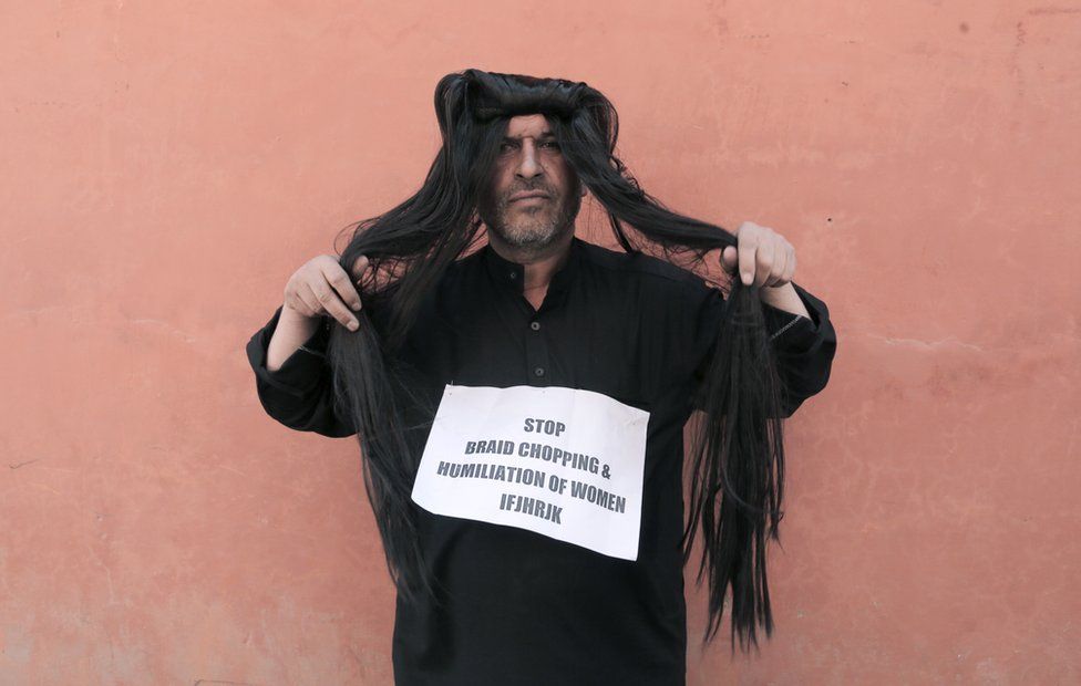 Ahsan Antoo wears a wig of long hair while holding a sign that says "stop braid chopping and humiliation of women" in Kashmir