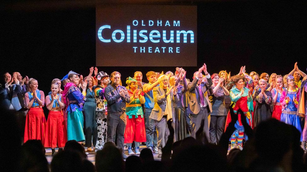 A crowd of performers gathered on the Oldham Coliseum stage in various costumes as the crowd applaud