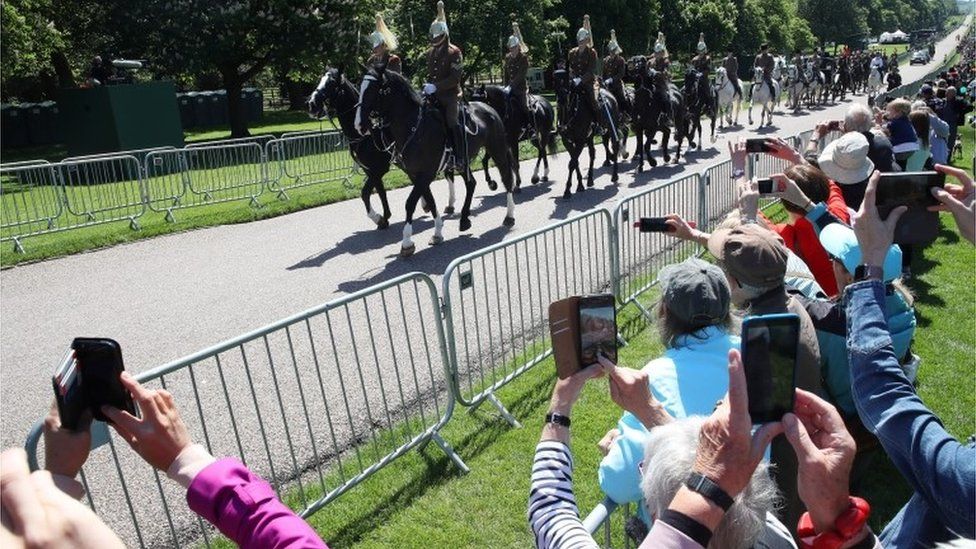 The household cavalry leads the procession as crowds capture them on their phones