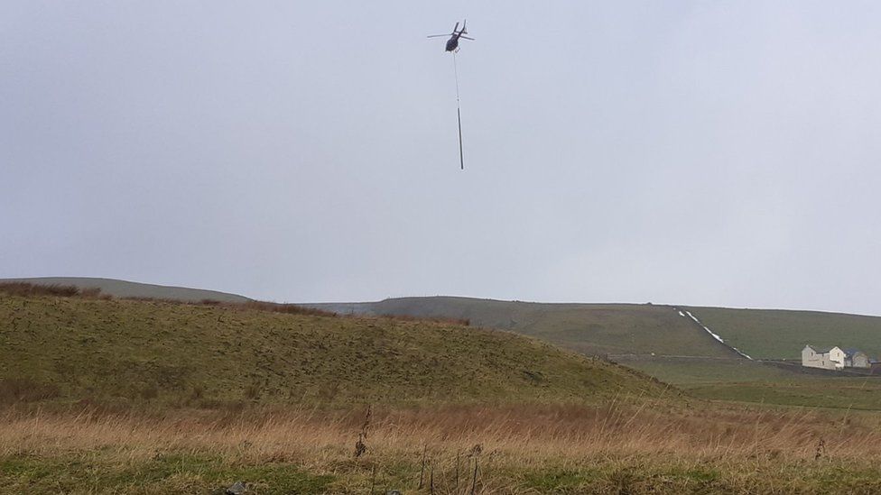 Helicopter carries new pole above countryside