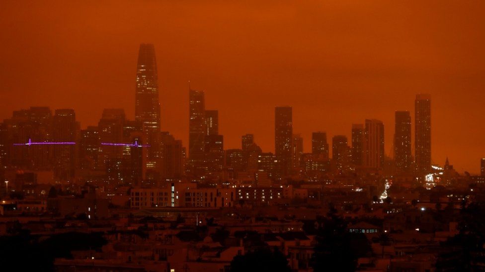 Downtown San Francisco is seen from Dolores Park under an orange sky