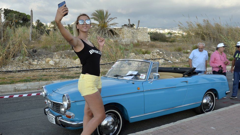 A Lebanese woman takes a selfie posing next to a 1968 Peugeot 404 convertible during the Classic Cars Show in Beirut