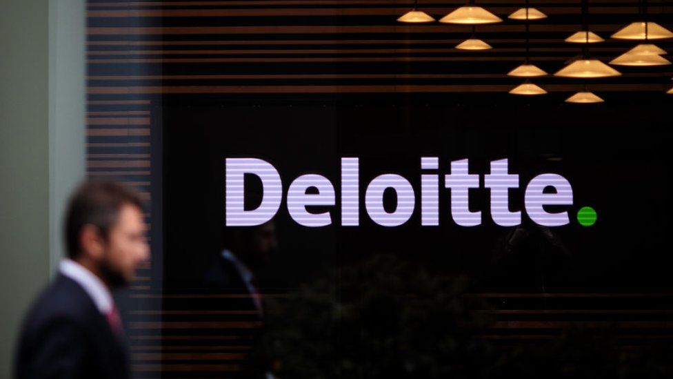 An anonymous man wearing a suit walks past the Deloitte offices in London, UK.