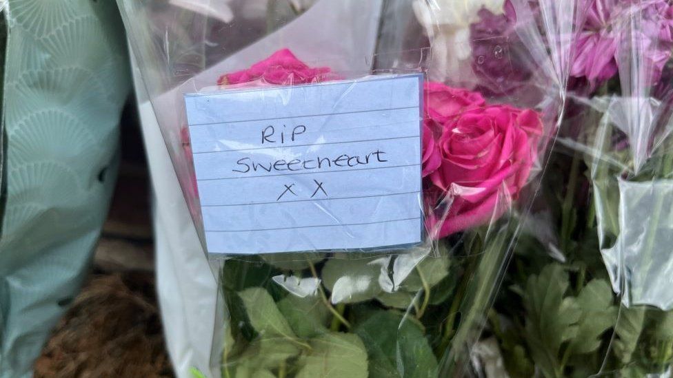 A note attached to some flowers reads 'RIP Sweetheart'.