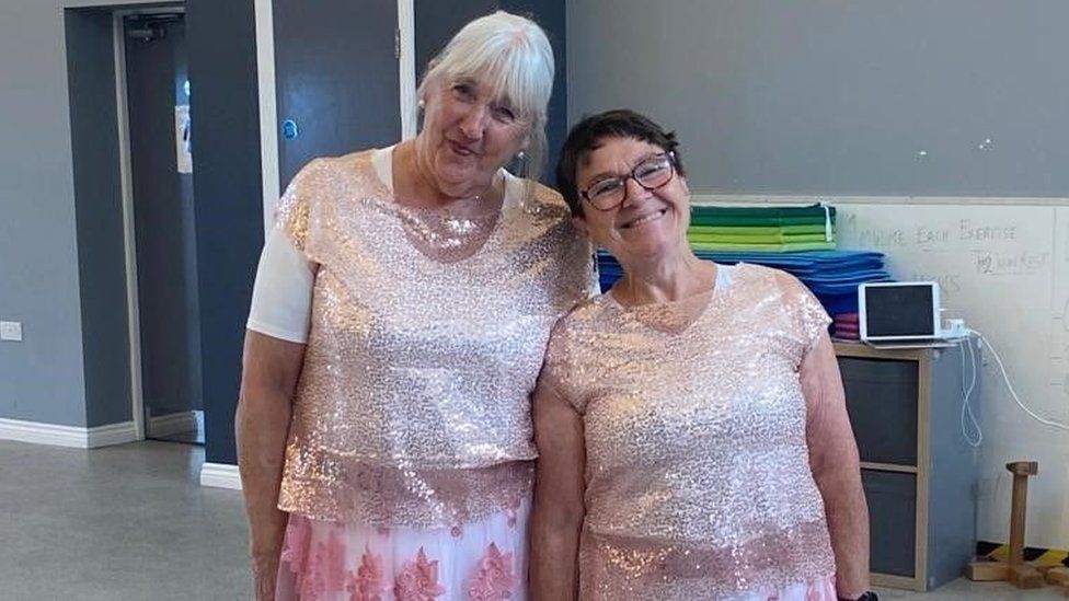 Two women in sparkly pink dresses smile at the camera