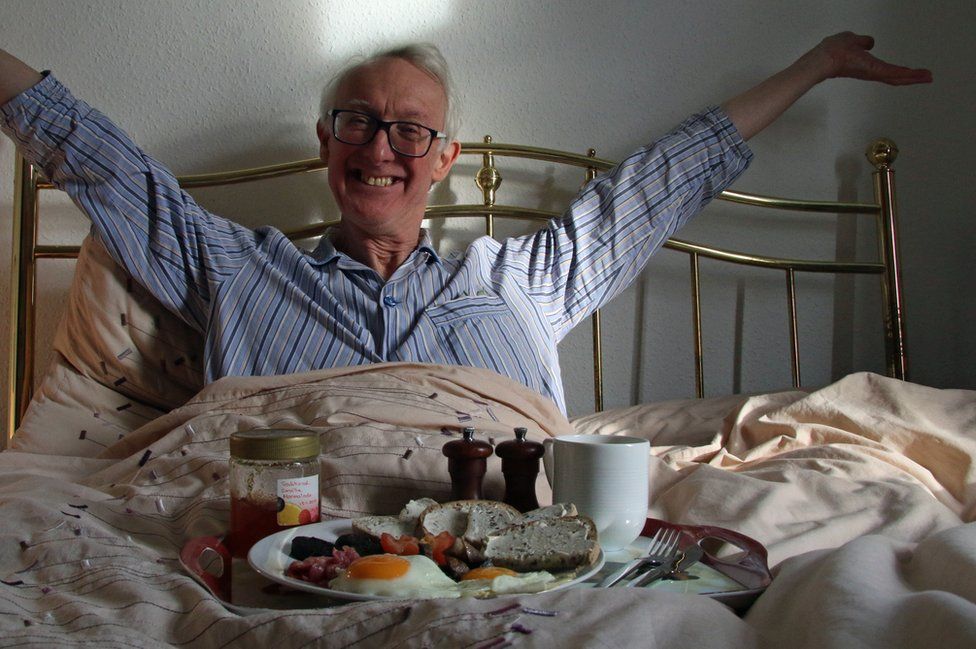 An older man eats breakfast in bed.