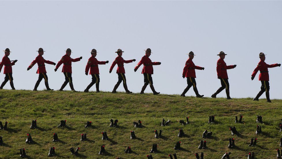 Royal Canadian Mounted Police officers marching past boots placed at the site