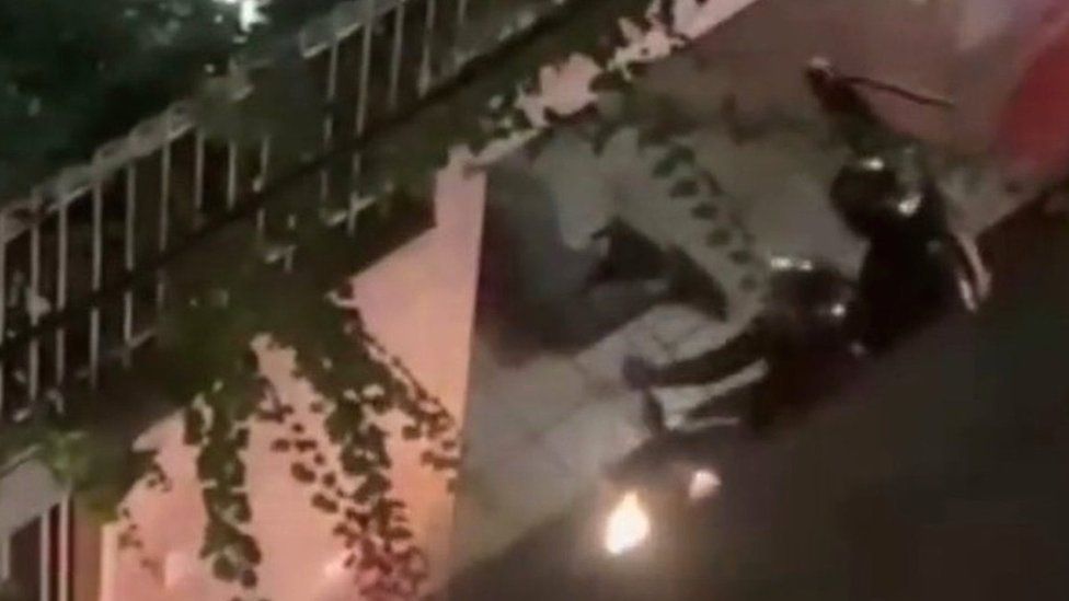 Скриншот видео, на котором иранский офицер полиции по охране общественного порядка поднимает дубинку перед тем, как избить лежащего на улице человека в Тегеране, Иран