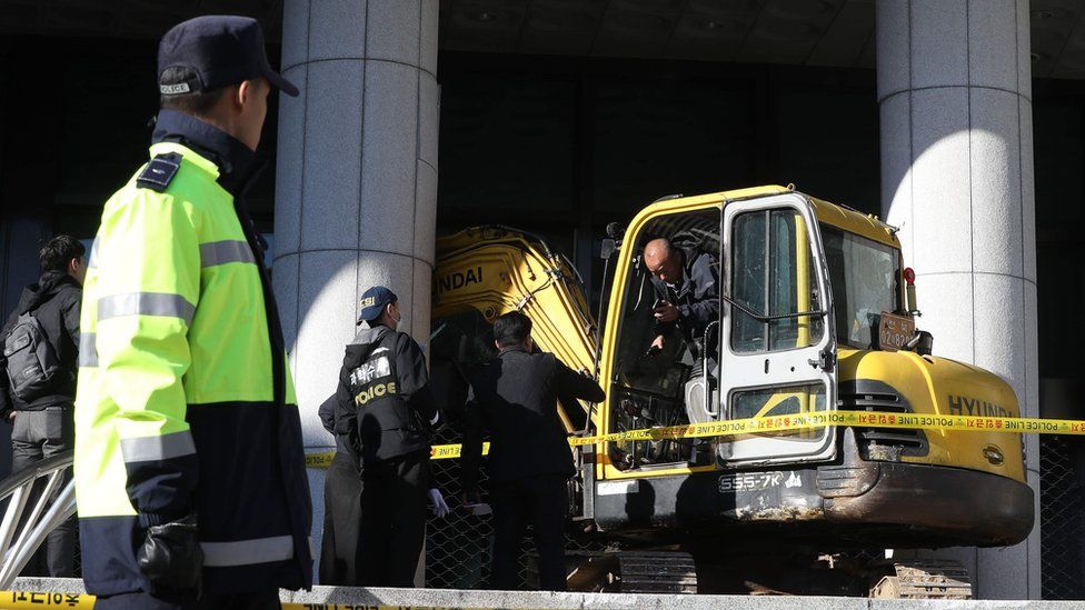 Policemen inspect an excavator after its driver attempted to ram the Seoul Central District Prosecutor's Office