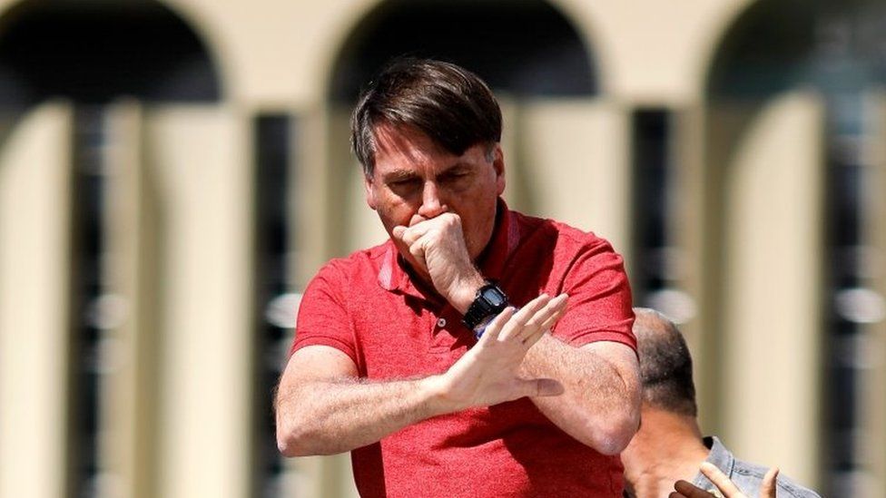 Brazilian President Jair Bolsonaro coughs as he speaks after joining his supporters who were taking part in a motorcade to protest against quarantine and social distancing measures to combat the new coronavirus outbreak in Brasilia on April 19, 2020