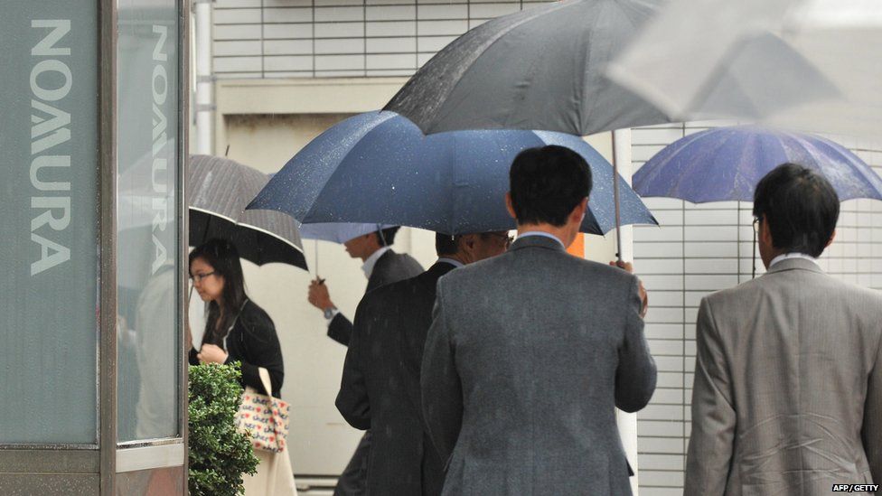 Pedestrians walk past signage of Nomura Securities in front of its branch in Tokyo