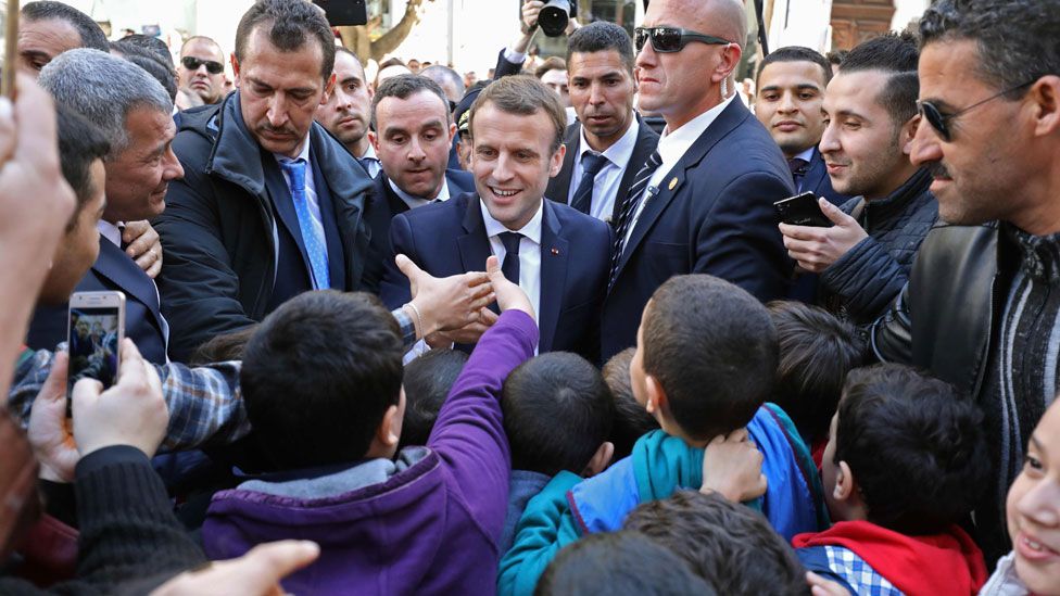 French President Emmanuel Macron is surrounded by security as he greets children in the streets of Algiers, Algeria- Wednesday 6 December 2017