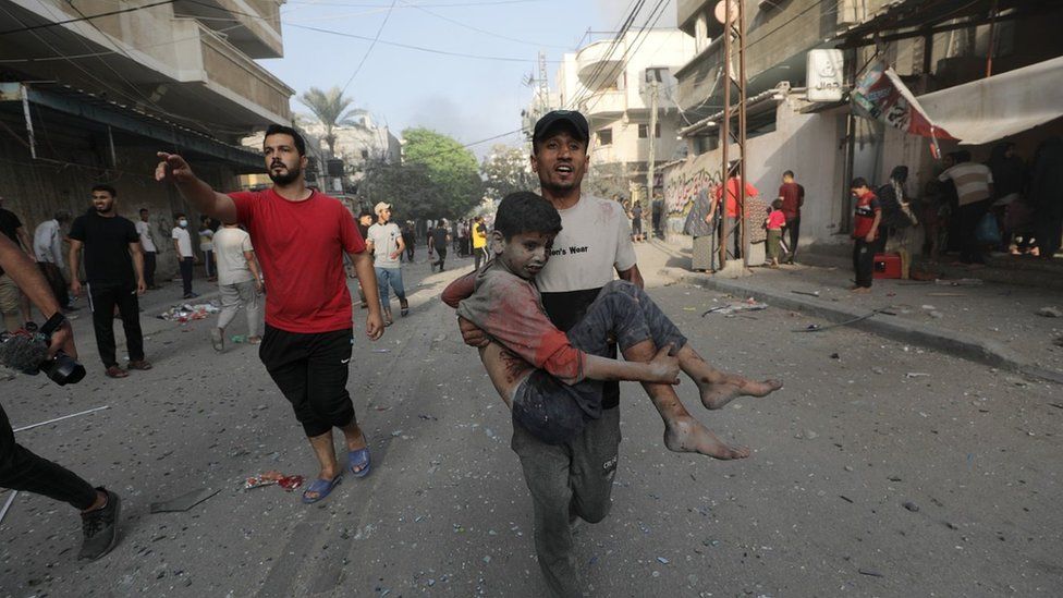 A Palestinian man carries a wounded boy following an Israeli air strike in northern Gaza (28 October 2023)