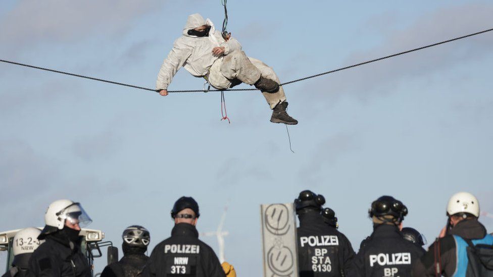 A activist hangs above riot police at the settlement of Luetzerath next to the Garzweiler II open cast coal mine on January 11, 2023