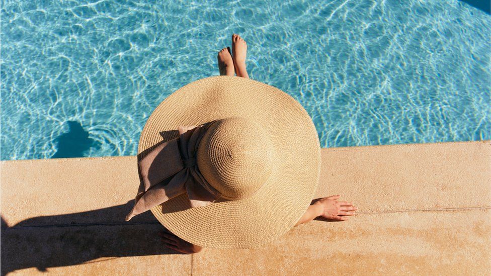 Sun bather in wide-brimmed hat sits next to pool