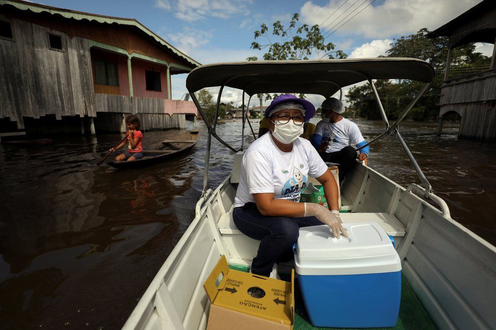 Municipal health worker Neuda Sousa is seen in a boat with a box of the Oxford/AstraZeneca vaccine against the coronavirus disease on a street a flooded by the rising Solimoes river