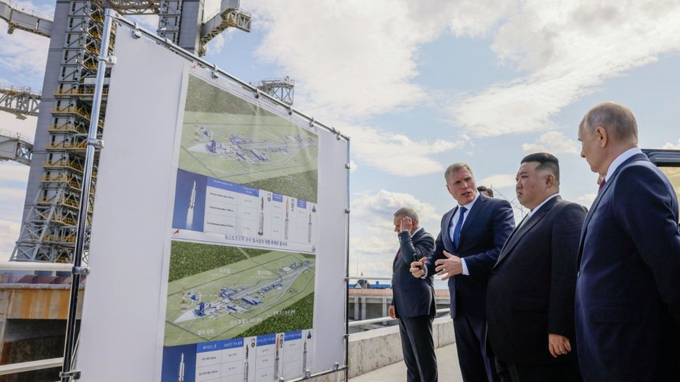 An official explains the base to both Kim and Putin as they stand in front of a map labelled in Korean