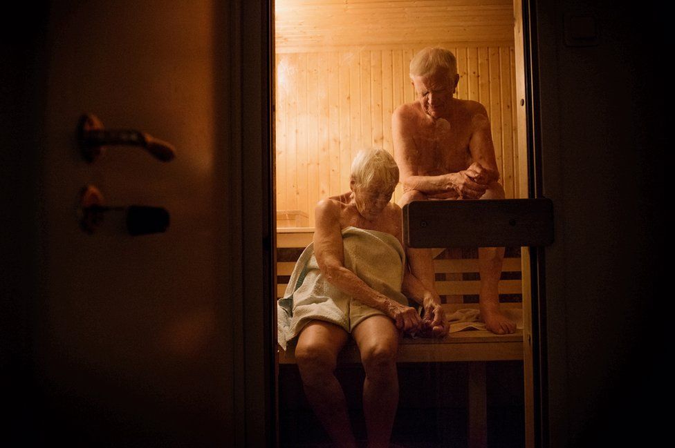 An elderly couple sit in a sauna.