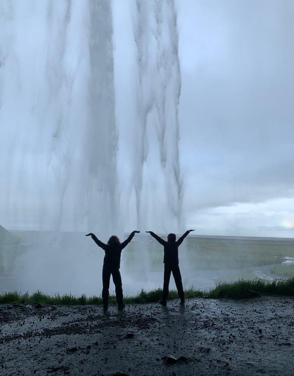 Two sisters pose as a waterfall pours in front of them