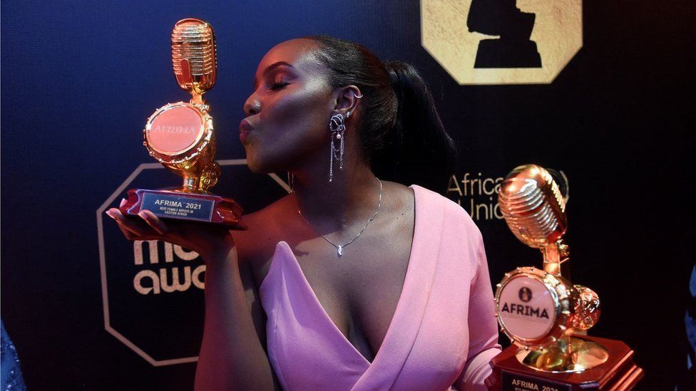 Nikita Kering wearing a pink outfit posing for a picture, kissing an award. She is holding another award in her other hand - Lagos, Nigeria Sunday 21 November 2021