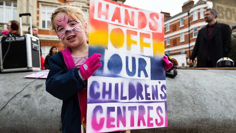 A young girl holds a placard as children and their parents stage a protest against the closure of Children's Centres in London.