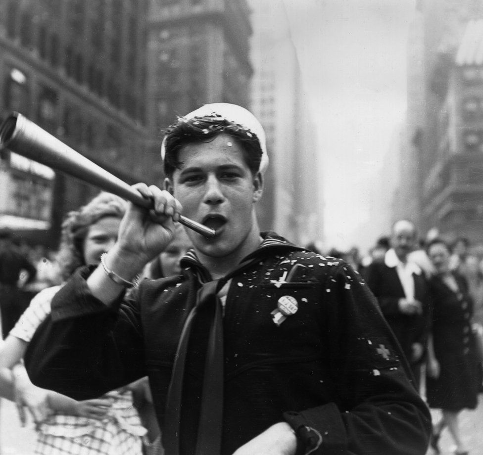 A sailor blows a trumpet in Times Square