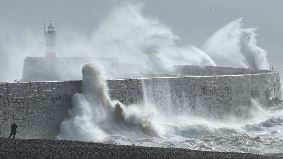 A person views as large waves hit the harbour wall at sunrinse during Storm Isha in Newhaven, southern Britain, on 22 January 2024