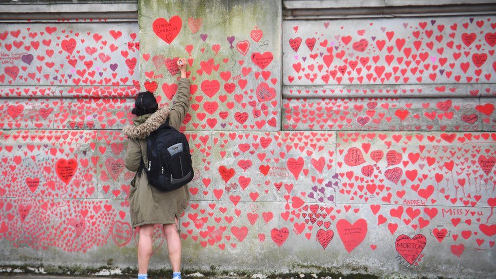 A person writes in a heart on the National Covid Memorial Wall on the Embankment in London