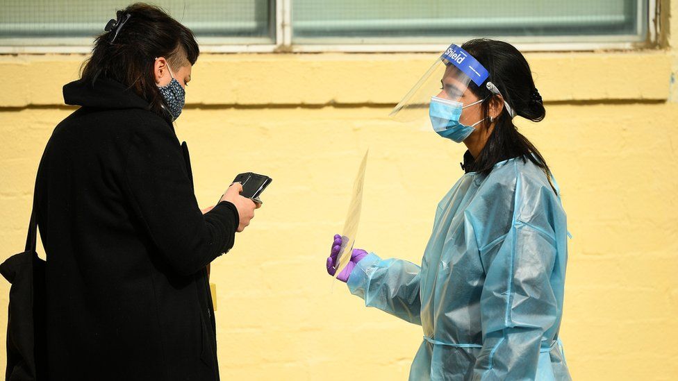 Медицинский работник в полном защитном снаряжении держит табличку с женщиной у входа в клинику
