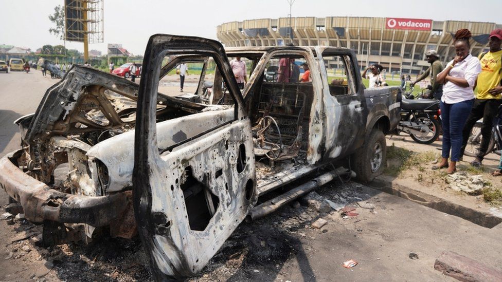People inspect a burned police car, after two groups of Muslims clashed outside Martyrs' Stadium in Kinshasa, Democratic Republic of Congo - 13 May 2021