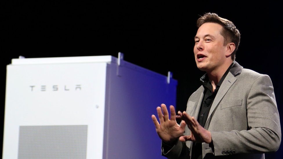Elon Musk, right of frame, stands near a large rectangular Tesla-branded white power storage unit on stage during a 2015 press event