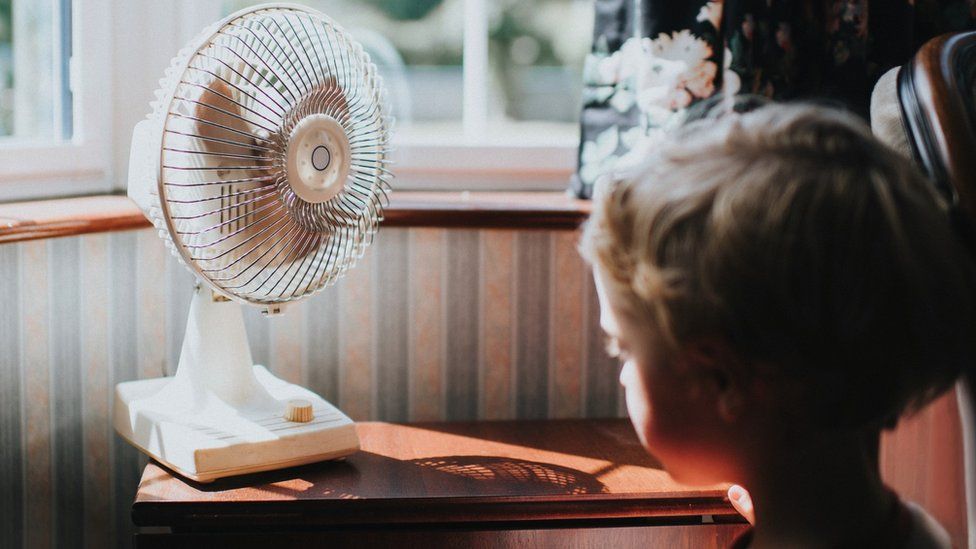 Boy sitting in front of a fan