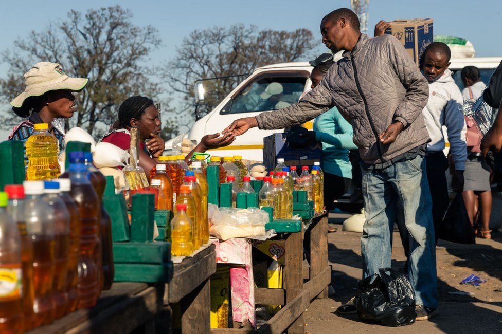 A customer buys cooking oil at a stall where smaller than standard measures of cooking oil is sold at Harare Mbare Musika marketplace in 2019.