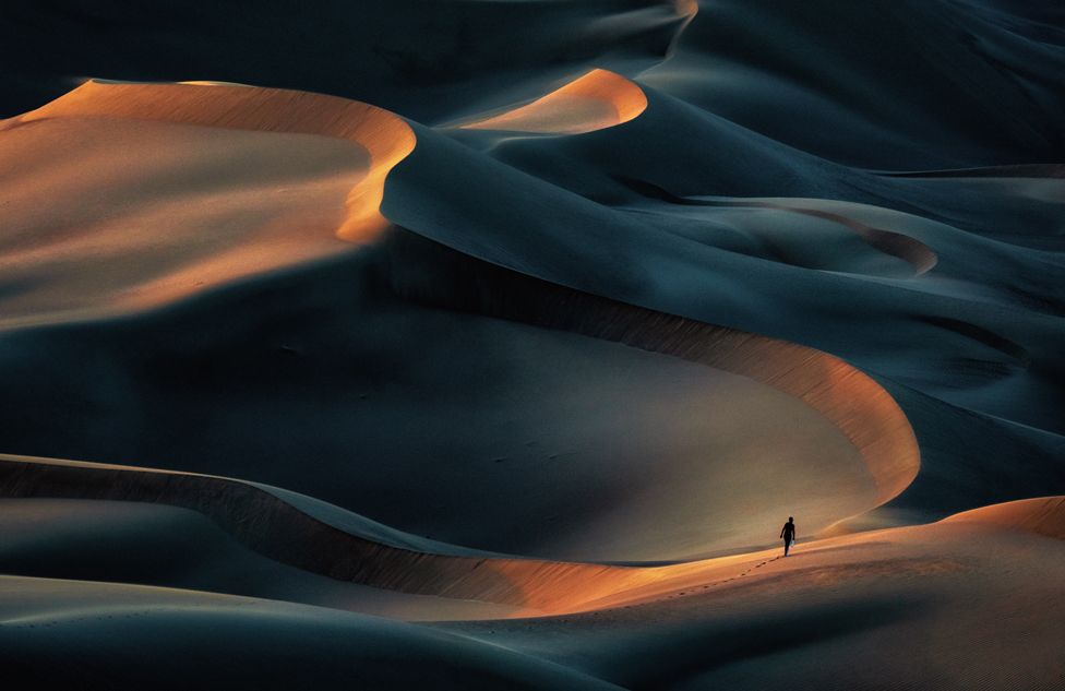 Distant figure walking across sand dunes