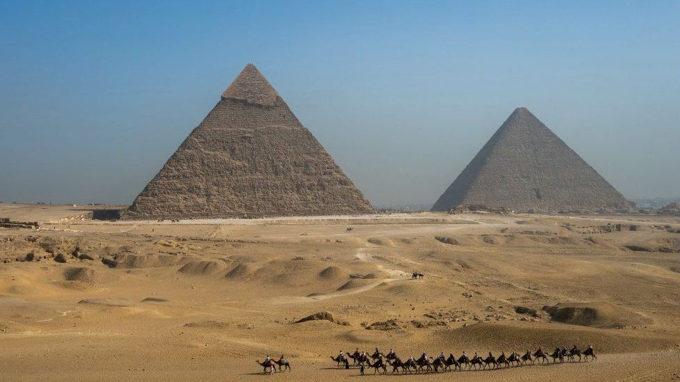 Tourists ride camels past the Great Pyramid of Khufu