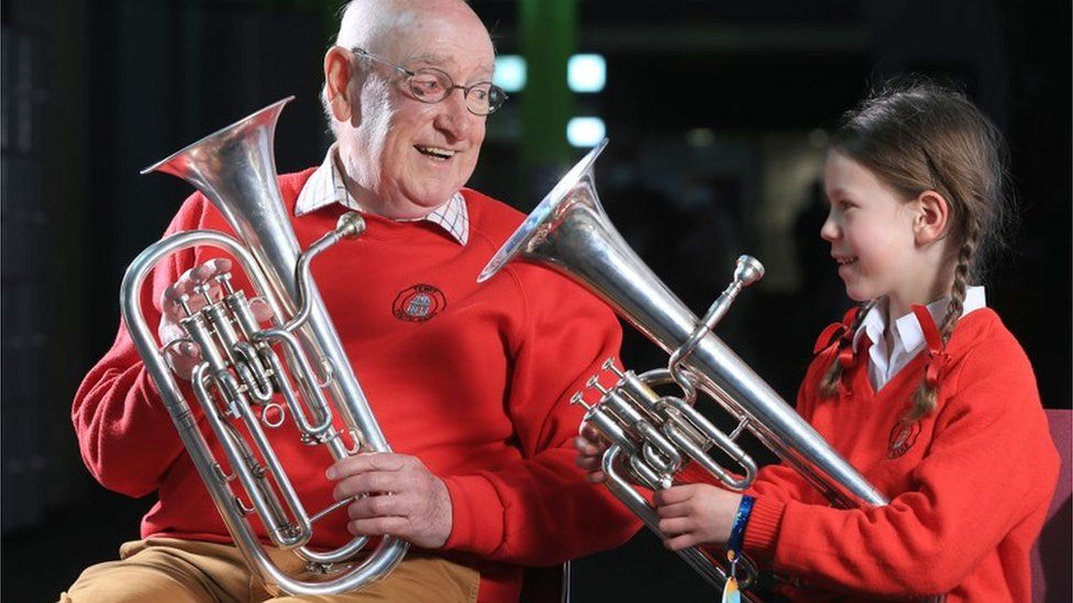 Elderly man playing alongside primary school pupil in a brass band