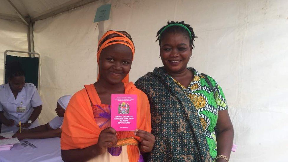 A girl who has been immunised poses with her vaccination booklet