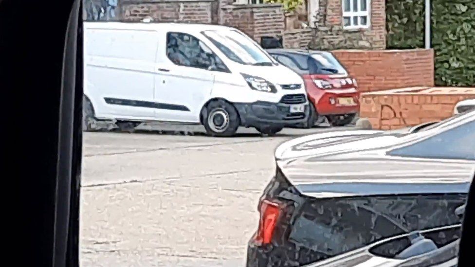 A white van with two other cars in the background