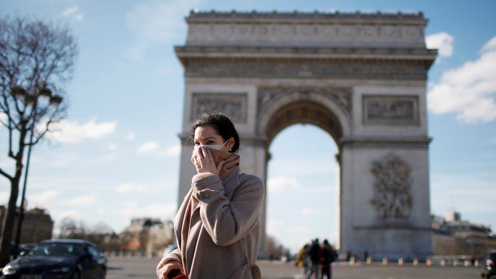 A woman wearing a protective mask walks near the Arc de Triomphe in Paris, 15 March