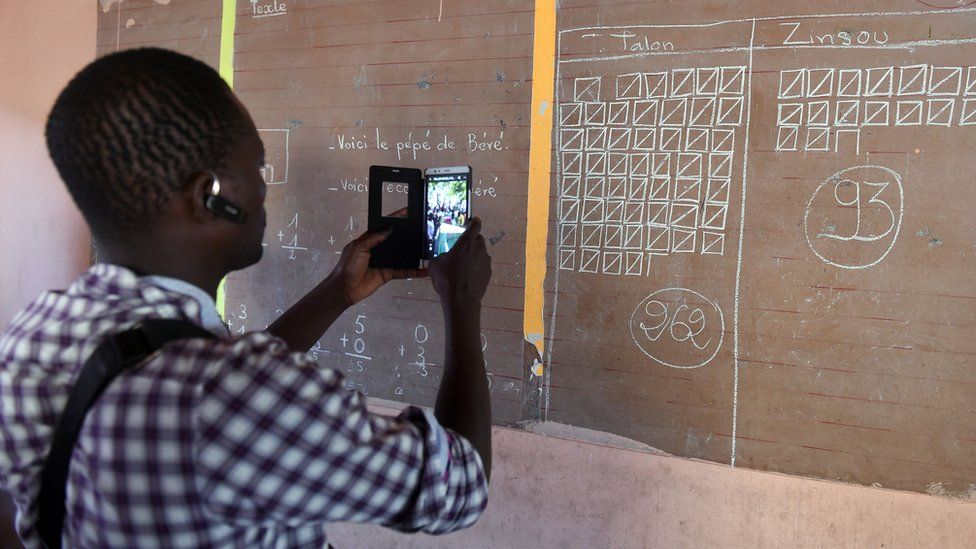 A man uses his phone to record the total votes cast in a polling station in Cotonou, Benin, 20 March 2016
