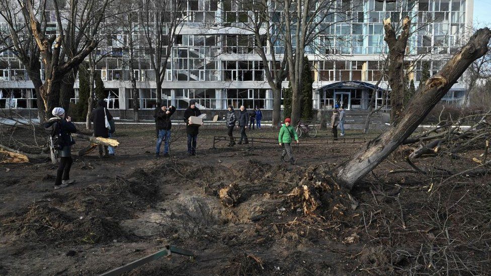 Bystanders look at a crater next to an educational building damaged the previous day by a missile strike in Kyiv